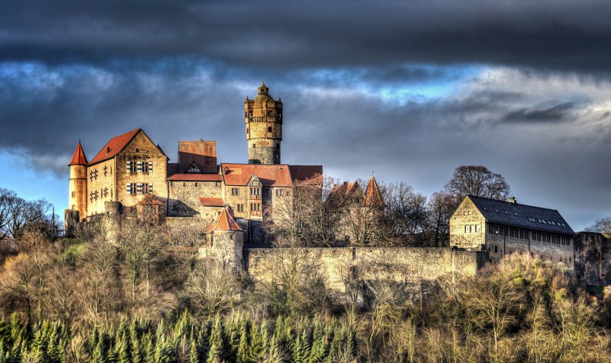 A historic hilltop castle under a dramatic cloudy sky