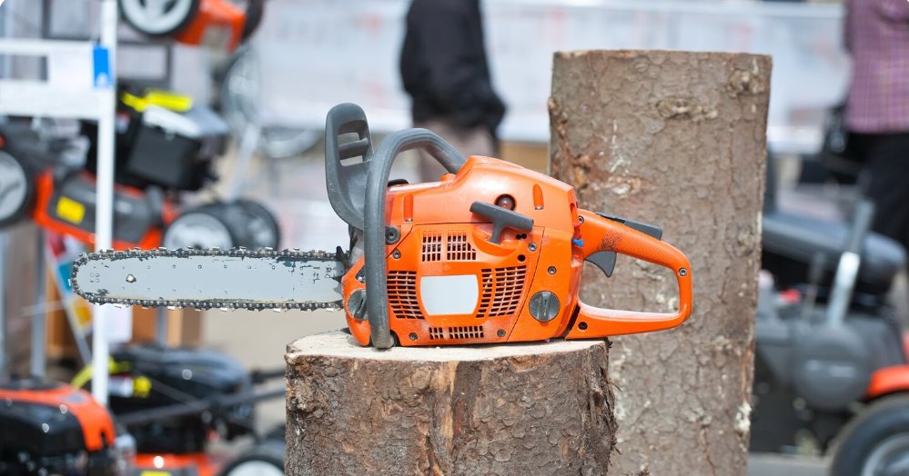 An orange chainsaw resting on a cut tree stump